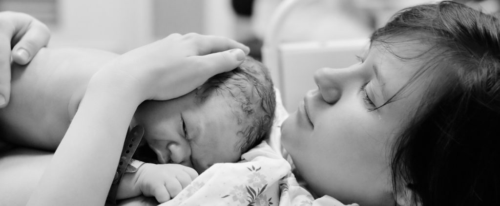 Black and white shot of young woman with newborn baby right after delivery